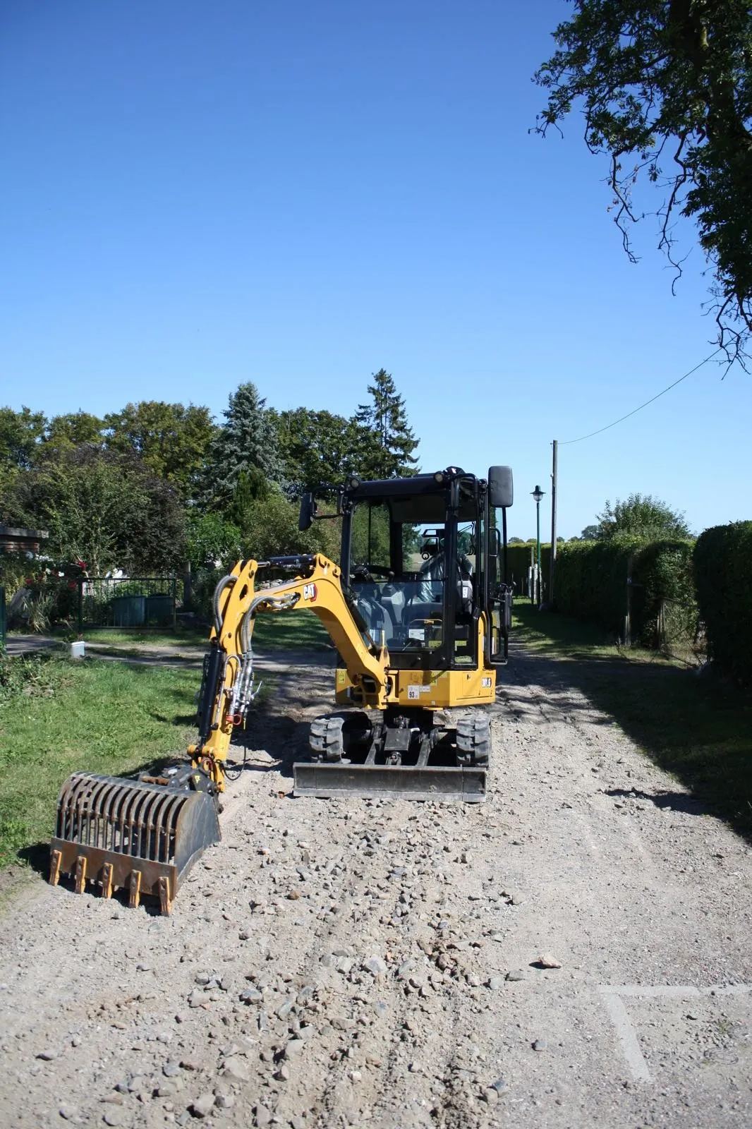 Mini-Bagger mit Planierschaufel auf einem Schotterweg